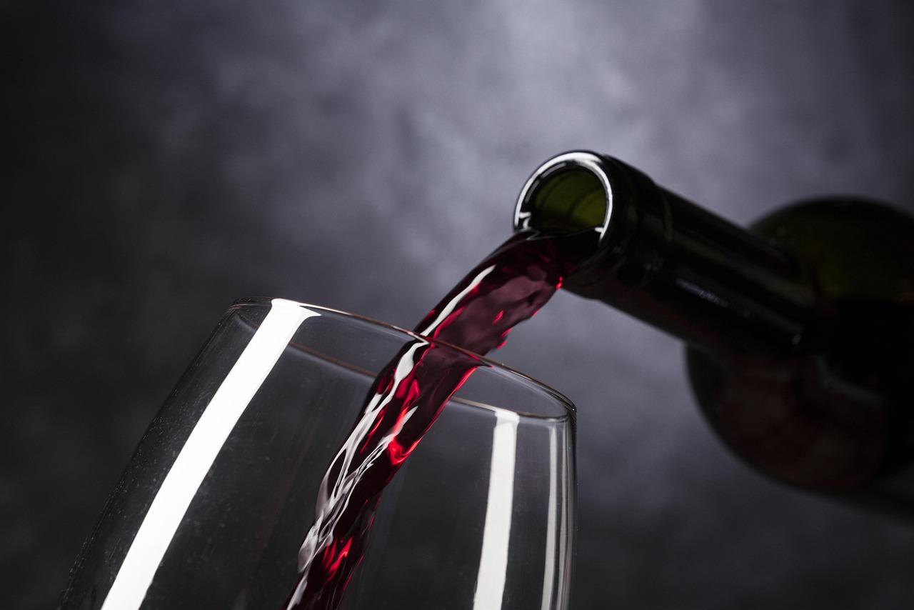 Servir vinho tinto de uma garrafa para um copo de vidro, com um fundo escuro